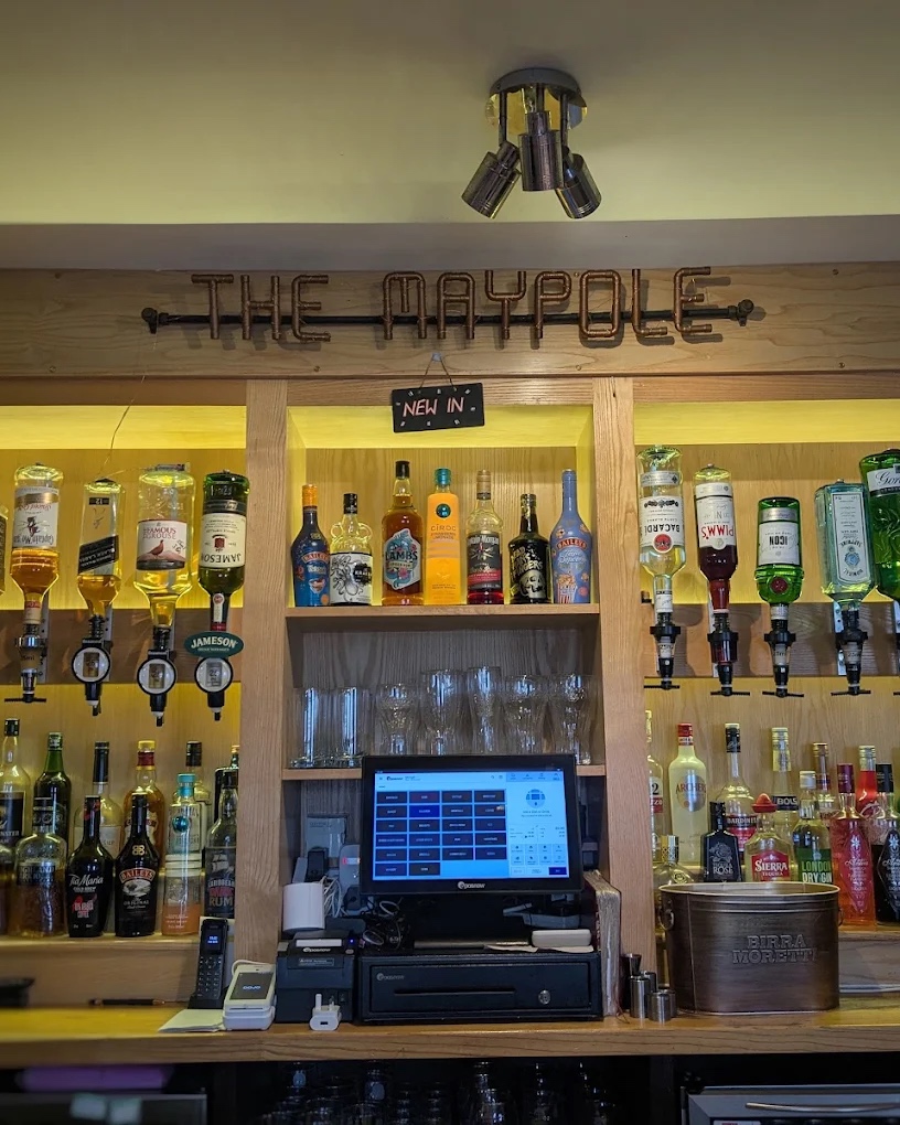 The bar at The Maypole Inn, with the lit Maypole sign above the optics